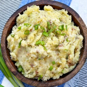 wooden bowl filled with red skin mashed potatoes flecked with chopped scallions