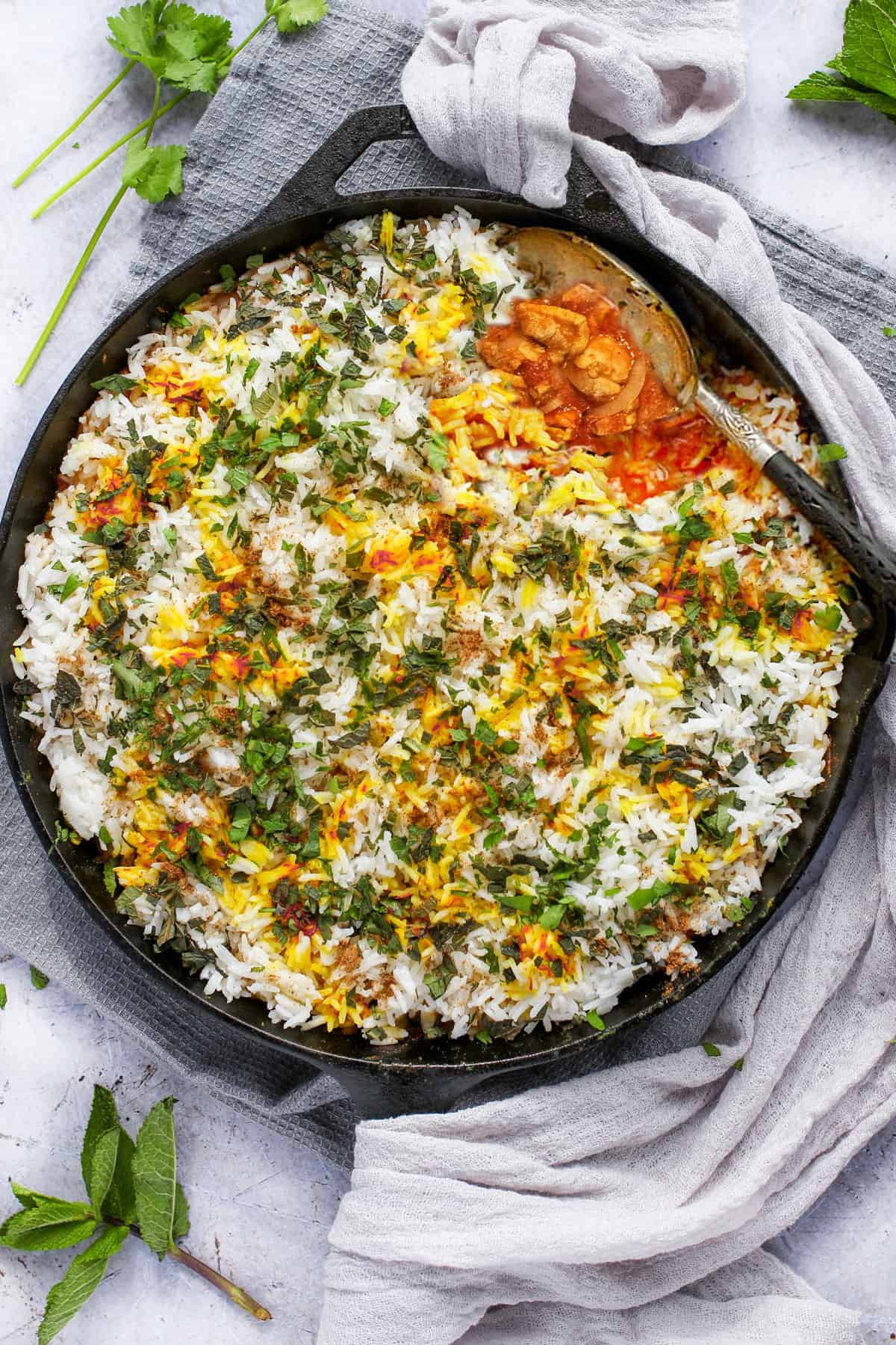 chicken biryani in a cast iron skillet with a serving spoon scooping sound out