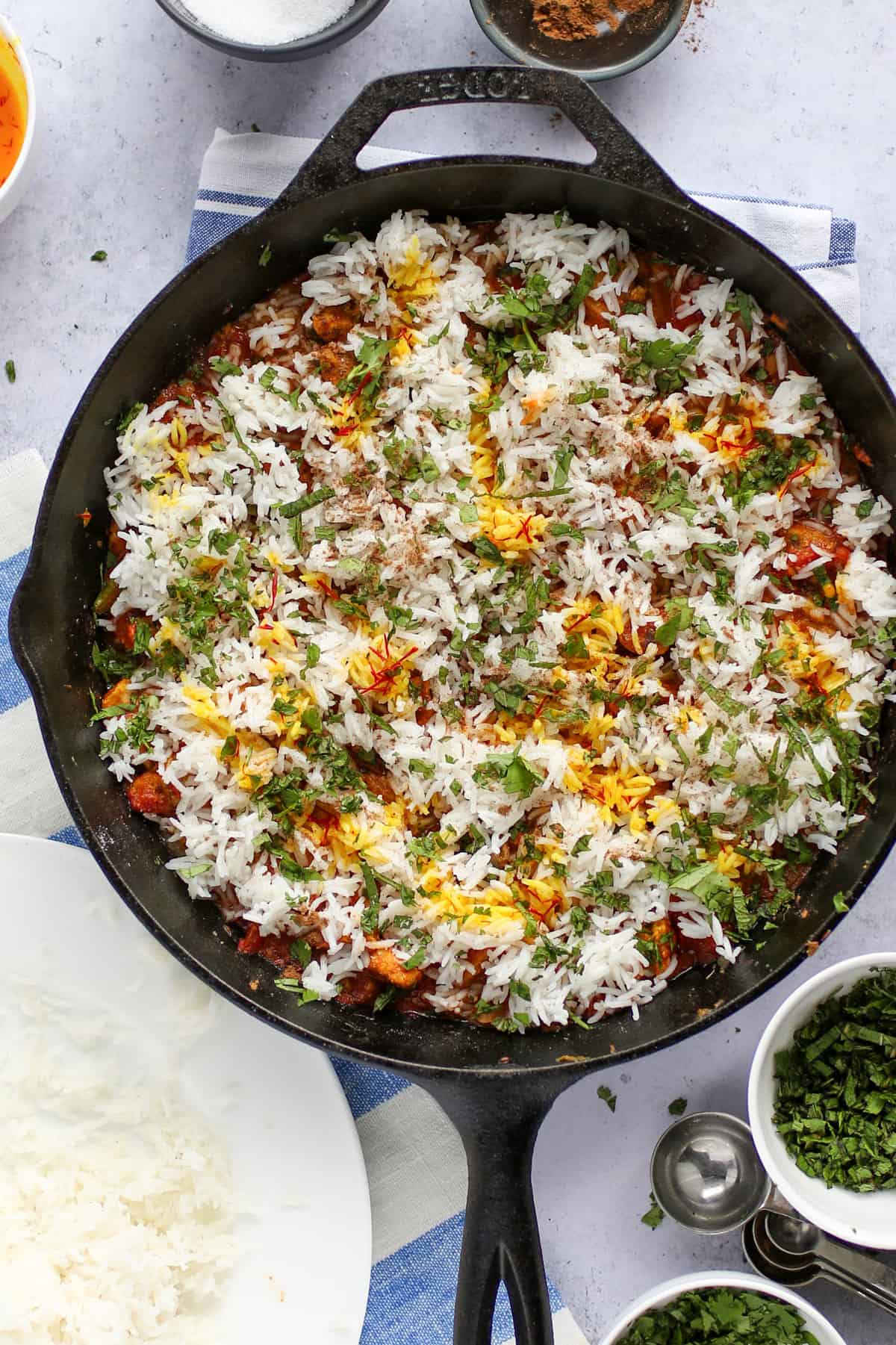 Cast iron skillet with fully assembled chicken biryani, the rice layer on top sprinkled with herbs and drizzled with saffron milk