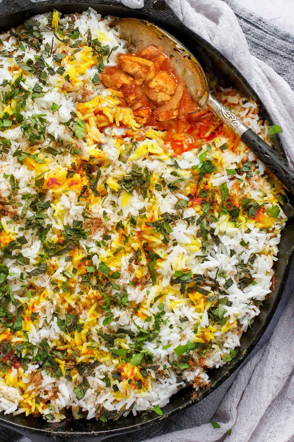 chicken biryani in a cast iron skillet with a serving spoon scooping some out