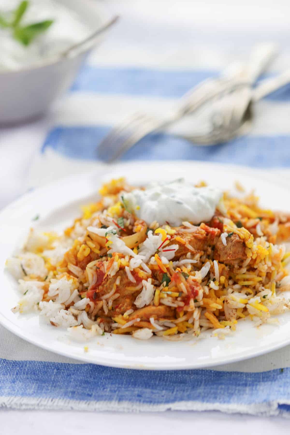 chicken biryani on a plate, topped with raita.