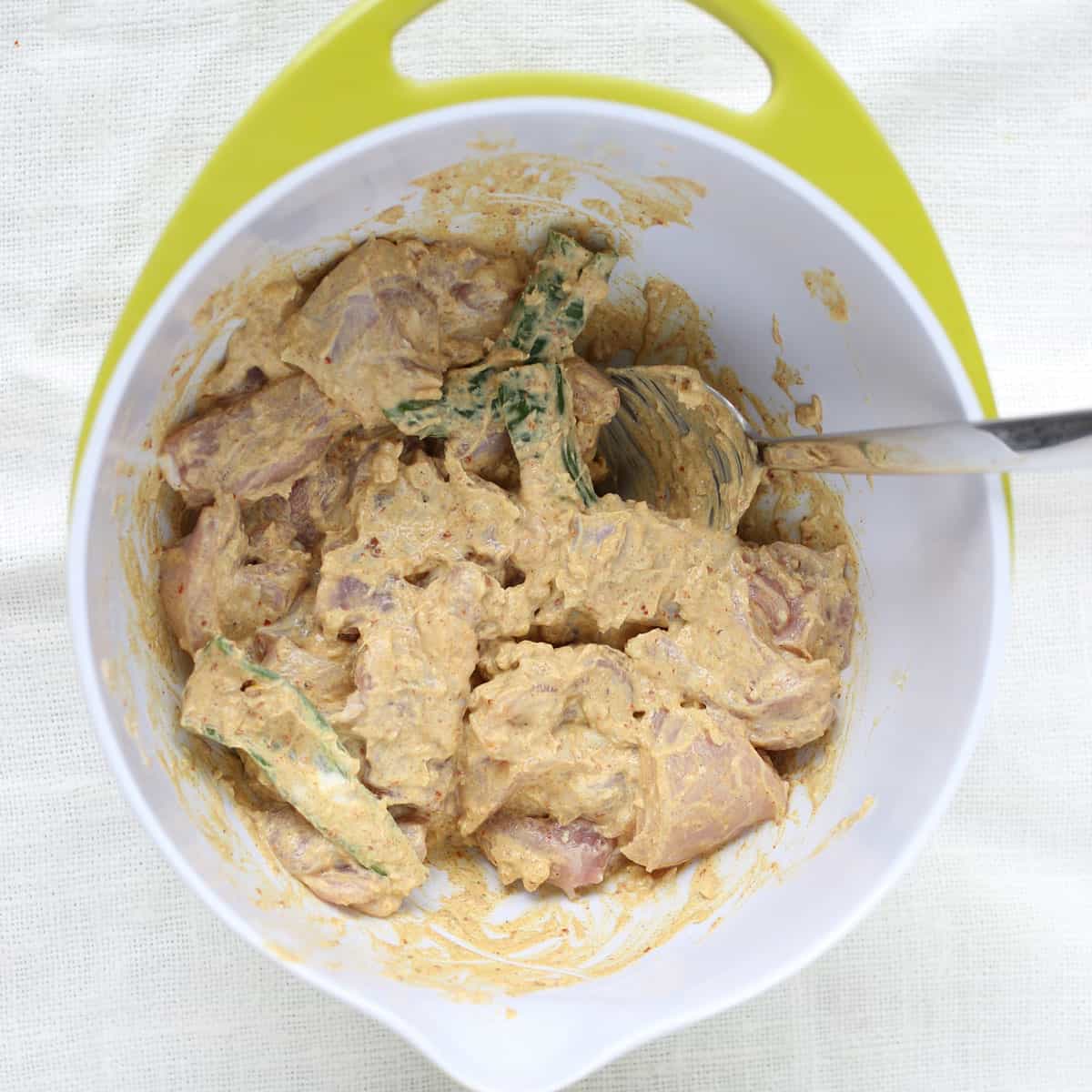 a mixing bowl filled with cubes of chicken in yogurt marinade