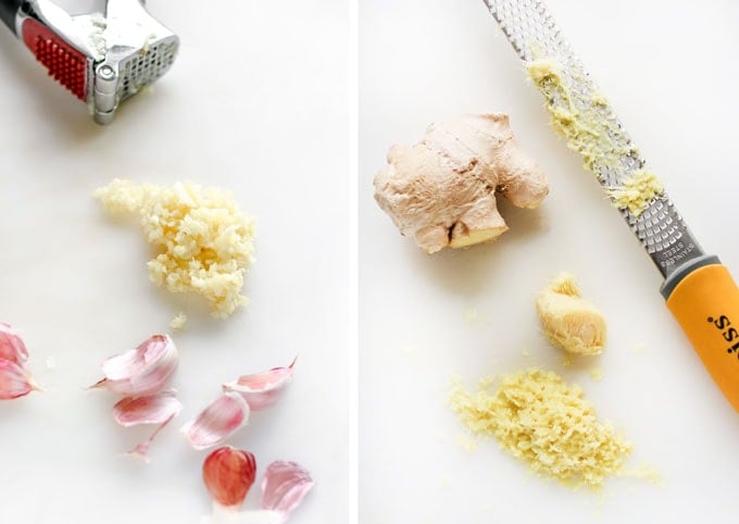 garlic press and pressed garlic on a countertop next to a grate and a hunk of ginger root and some grated ginger