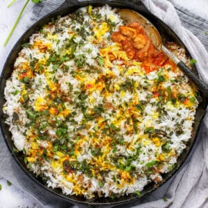 chicken biryani in a cast iron skillet with a serving spoon scooping some out