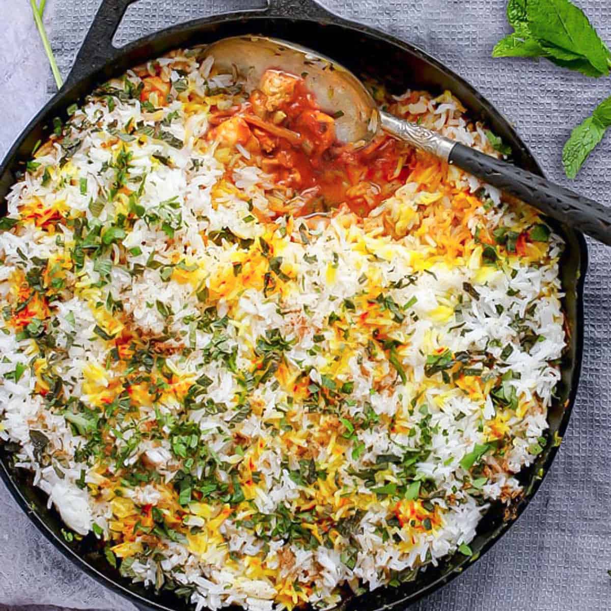 chicken biryani in a cast iron skillet with a serving spoon scooping sound out