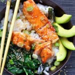 rice bowl with salmon teriyaki, sautéed spinach and sliced avocado, with chop sticks.