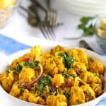 bright yellow turmeric cauliflower salad in a white bowl on a blue and white striped napkin with forks in the background