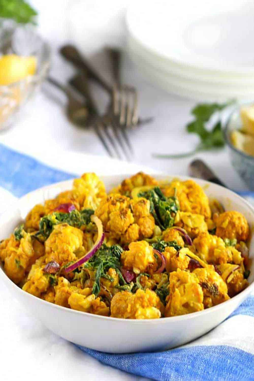 bright yellow turmeric cauliflower salad in a white bowl on a blue and white striped napkin with forks in the background