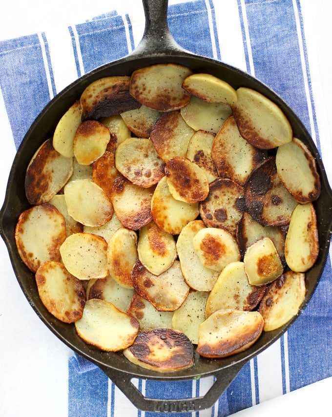 Sautéed potato slices line a cast iron skillet to forma potato crust for greek spinach pie