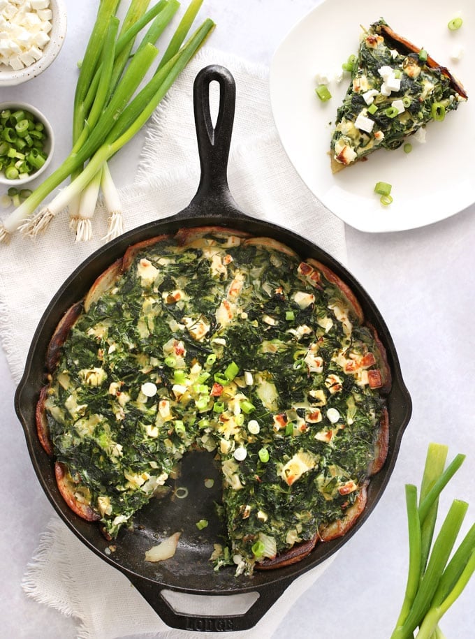 a cast iron skillet with Greek spinach pie in potato crust and a slice of pie on a plate