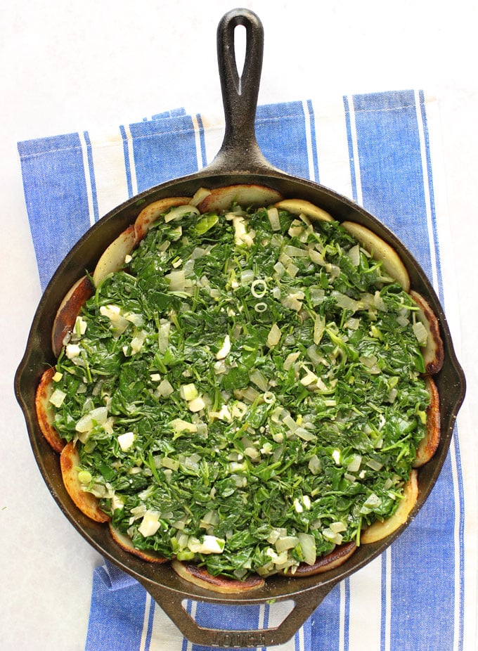 A cast iron skillet with crust and filling for Greek spinach pie with potato crust