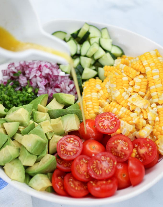 Pouring dressing on ingredients for corn, tomato, avocado salad