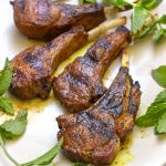 4 grilled lamb chops on a plate with mint sprigs