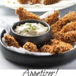 9 pieces of fried chicken fingers in a black bowl, with a small bowl of remoulade sauce to dip