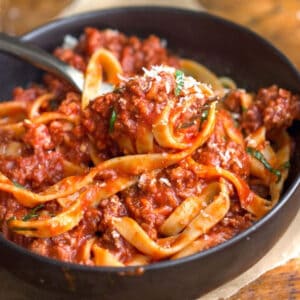 Bowl of fettuccini with thick tomato meat sauce swirled around a fork.