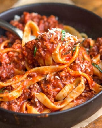 Bowl of fettuccini with thick tomato meat sauce swirled around a fork.