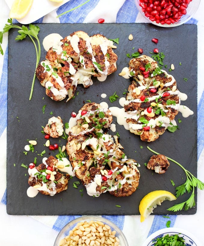 Cauliflower shawarma steaks on a platter with tahini and pomegranate seeds