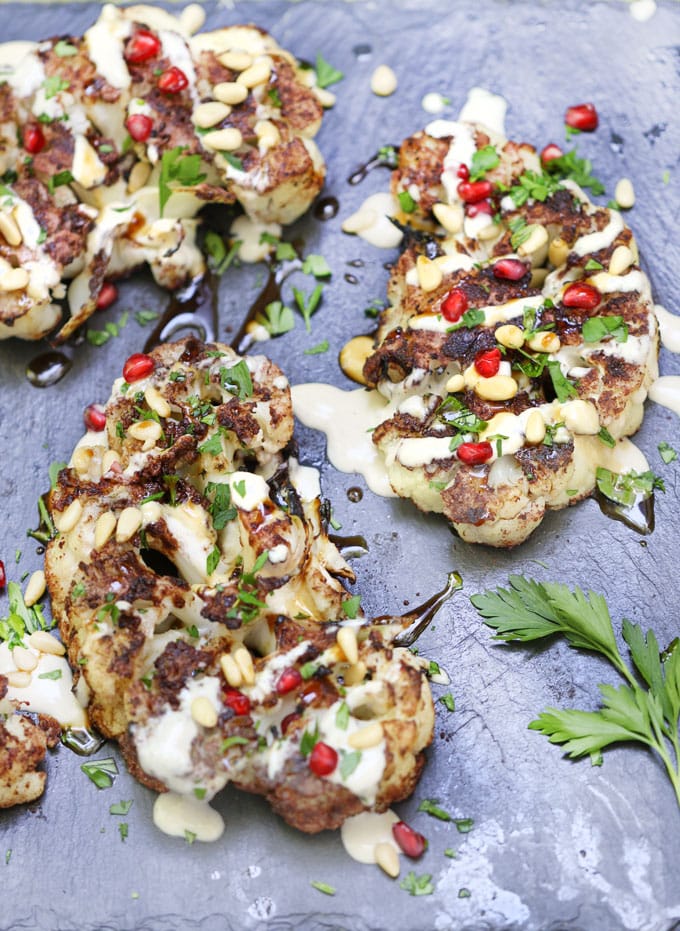 Cauliflower shawarma steaks on a platter with tahini and pomegranate seeds