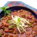 bowl of vegetarian chili topped with shredded cheese and chopped scallions.