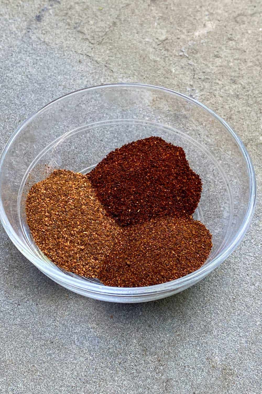 Three different chili powders, each a different shade of red, in a small glass bowl.