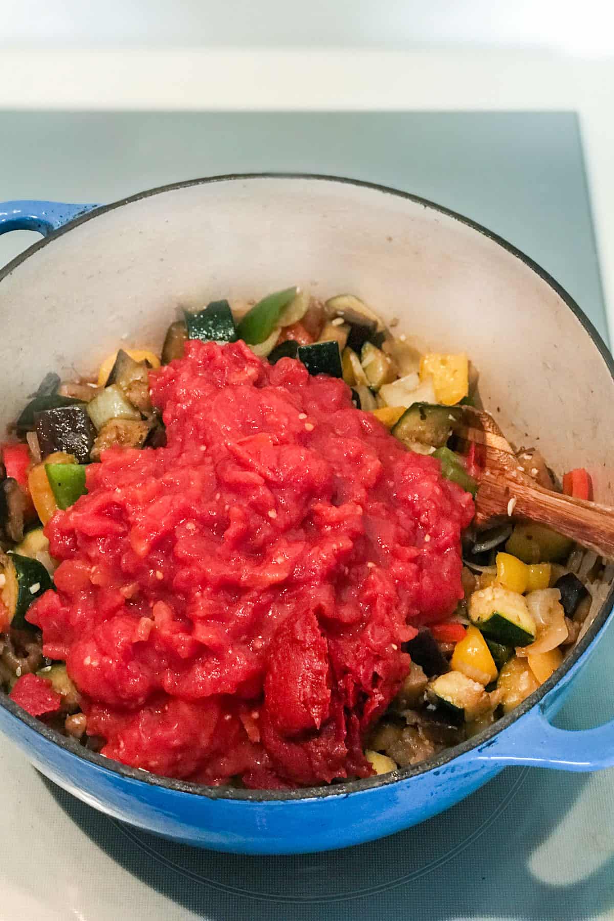 Crushed tomatoes and tomato pasted added to Ratatouille vegetables in a dutch oven