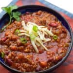 bowl of vegetarian chili garnished with shredded cheese and chopped scallions