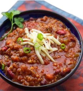 bowl of vegetarian chili garnished with shredded cheese and chopped scallions