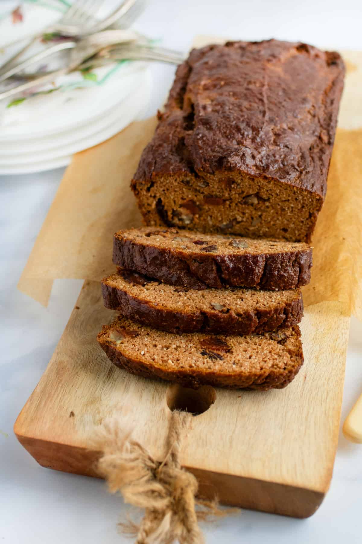 A loaf of pumpkin bread on a wooden board with three slices cut and leaning down from the loaf.