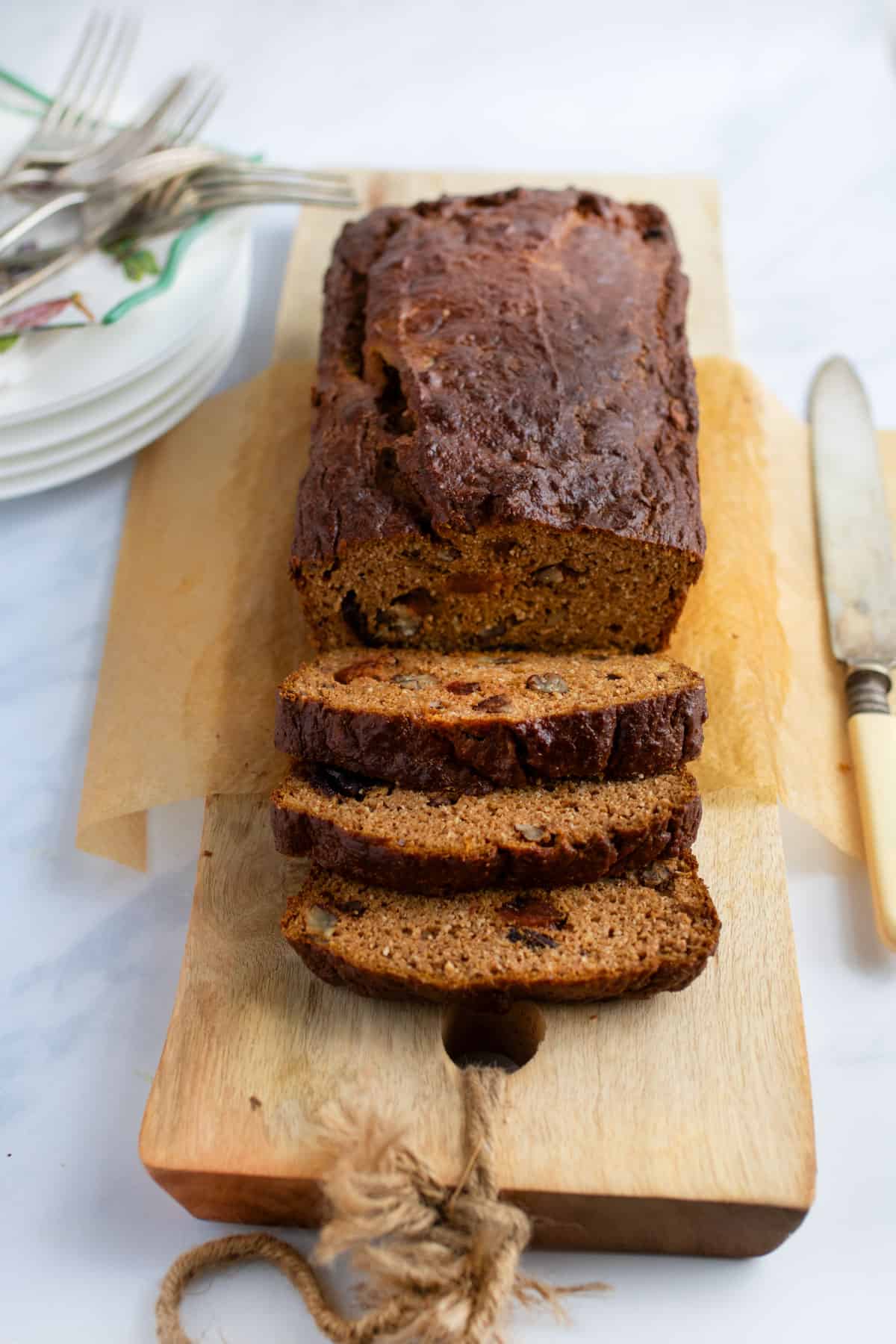 A loaf of pumpkin bread on a wooden board with three slices cut and leaning down from the loaf.