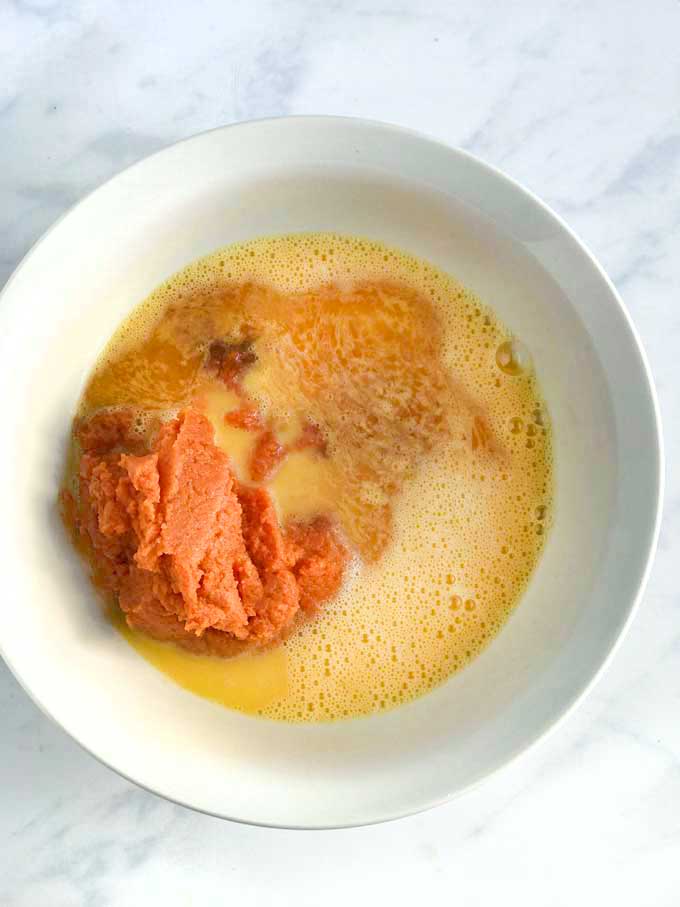 Ingredients in a bowl to make healthy pumpkin bread: eggs, pumpkin, maple syrup and vanilla