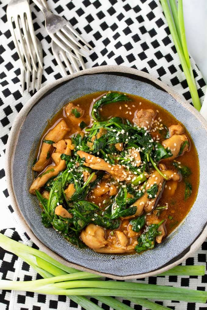 a blue bowl filled with a stew of chicken and spinach in gochujang sauce, sprinkled with sesame seeds