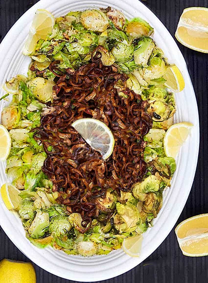 shredded Brussels sprouts on an oval platter topped with crispy fried shallots, a lemon wedge on top