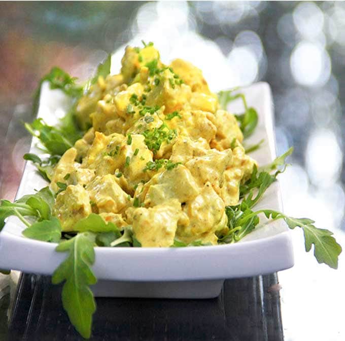 a big heap of bright yellow curried chicken salad on a rectangular platter with arugula leaves scattered around