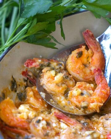 A pot of Greek lemon butter garlic shrimp with a serving spoon holding three of the shrimp