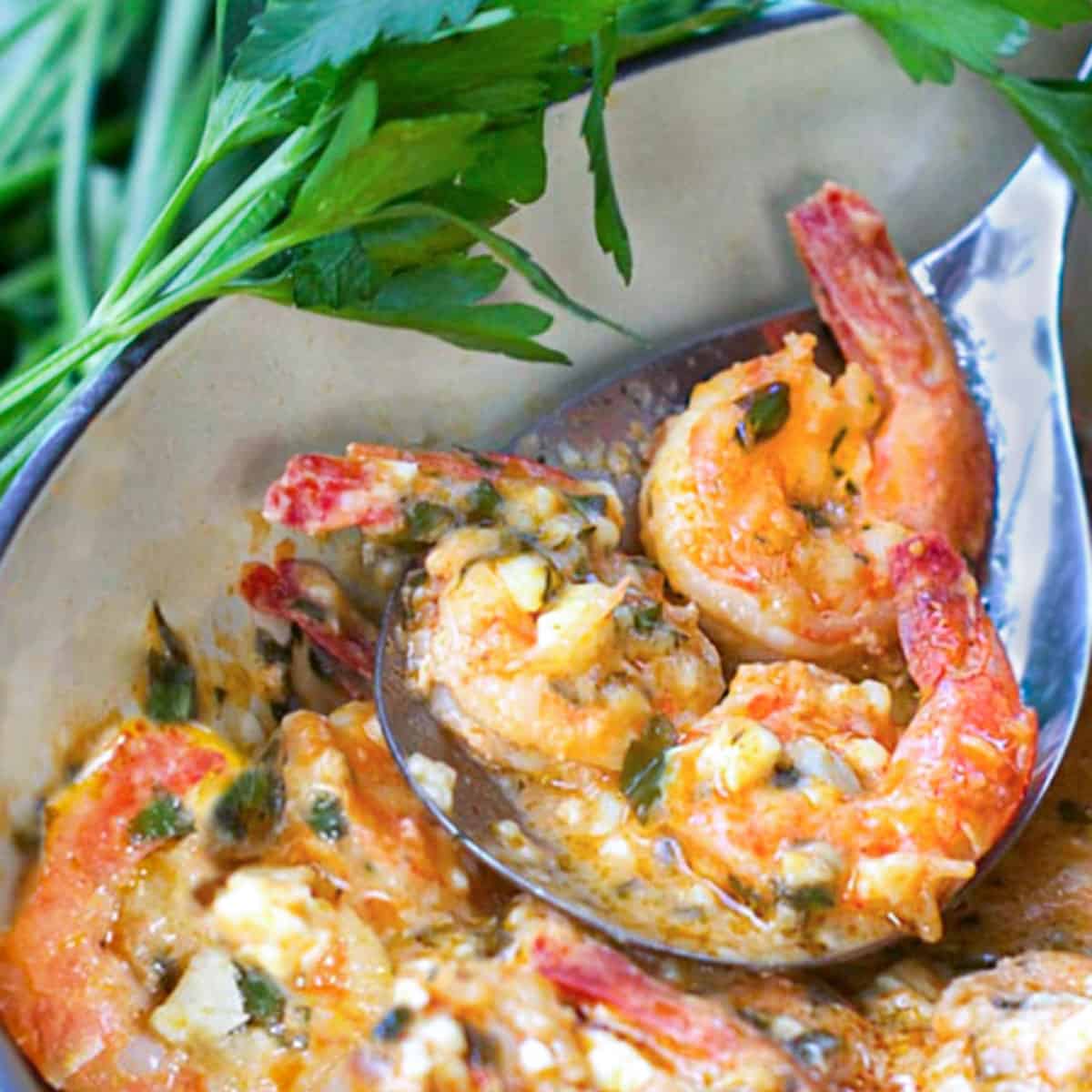 A pot of Greek lemon butter garlic shrimp with a serving spoon holding three of the shrimp