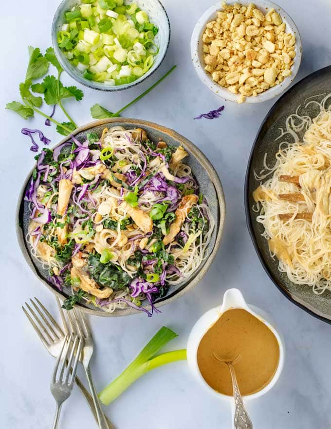 Thai Noodle Salad bowl surrounded by bowls of peanut dressing, chopped peanuts and chopped scallions