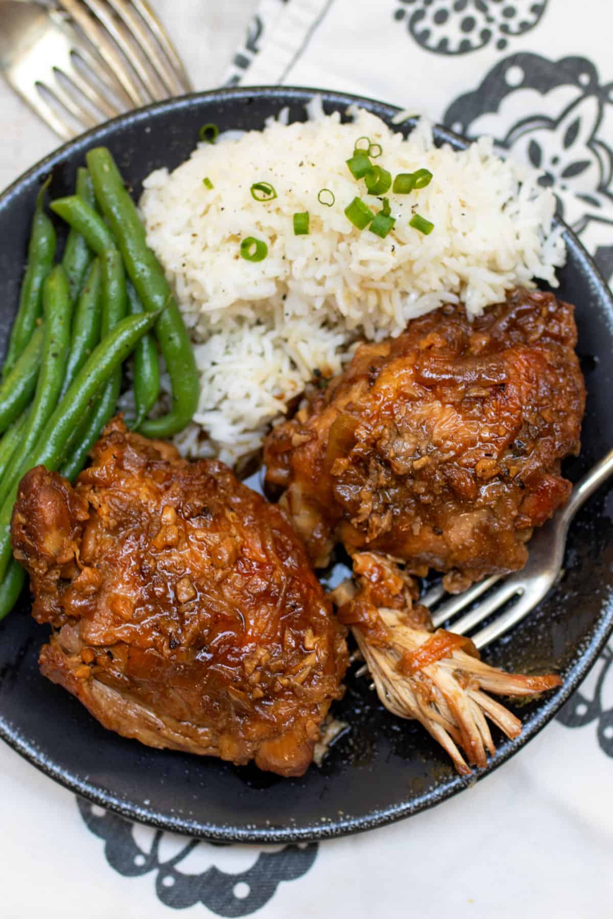 Plate with two pieces of braised chicken coated in rich sauce next to white rice topped with chopped scallions, and steamed green beans.