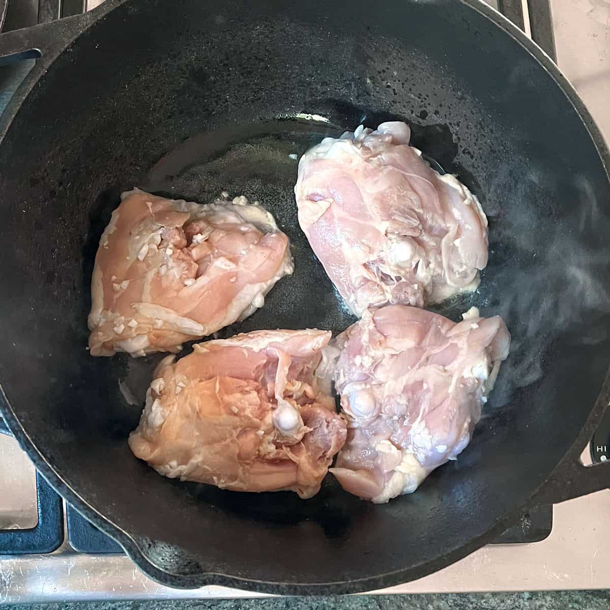 4 bone-in chicken thighs being seared in a large dutch oven.