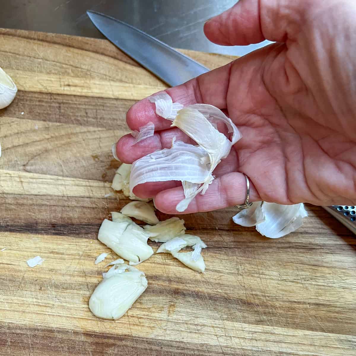 A hand holding the in-tact skin of a garlic clove.
