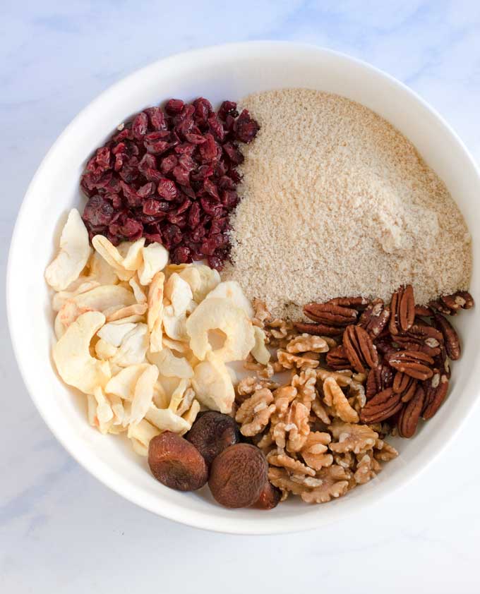 Big white bowl with dried cranberries, dried apple slices, almond flour, walnuts, pecans and dried apricots