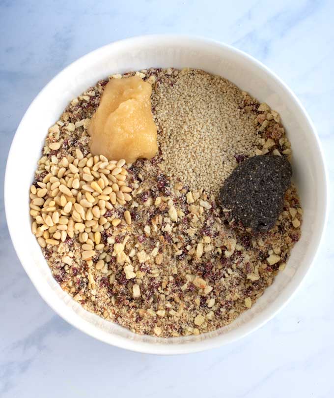 Big white bowl filled with ground dried fruits and nuts, raw honey, sesame seeds, chia seeds and pine nuts