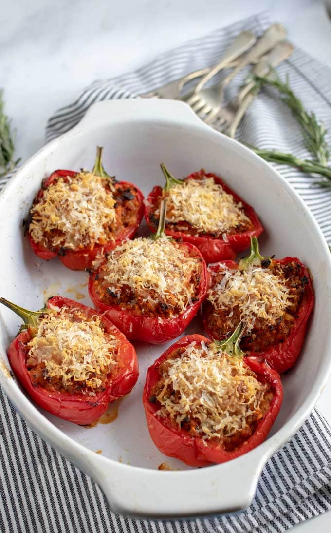6 stuffed red peppers filled with minced pork and topped with parmesan cheese. Forks and rosemary sprigs and a striped dish towel in the background 