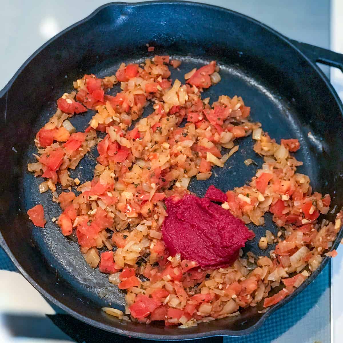 Tomato onions mixture in a cast iron skillet topped with tomato paste.