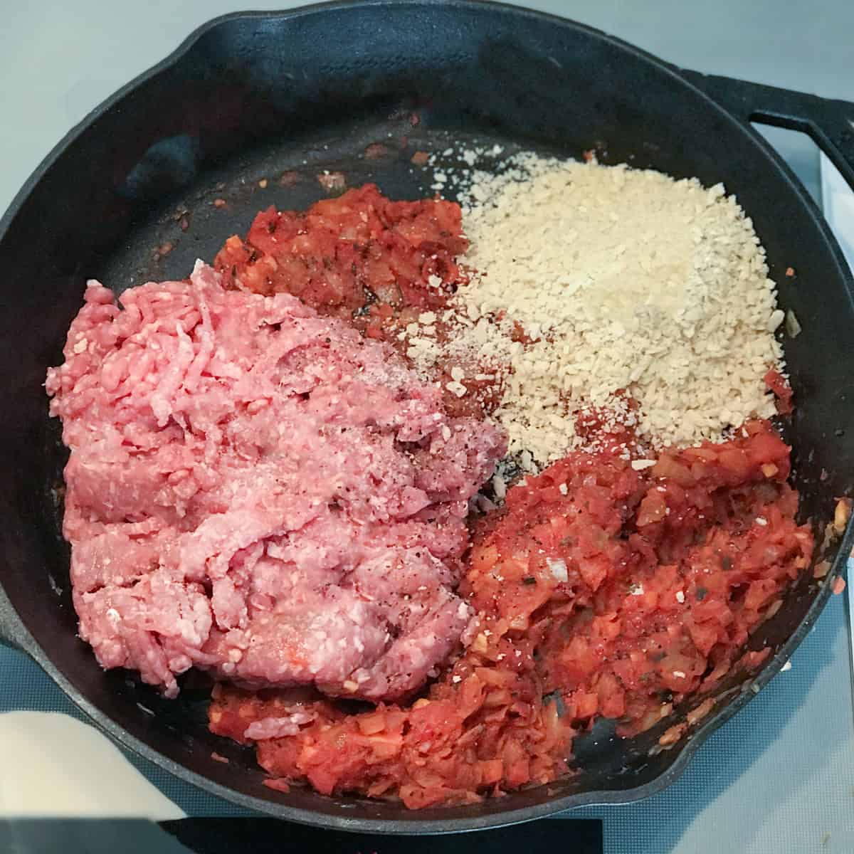 tomato mixture in a cast iron skillet along with some raw ground pork and panko bread crumbs.
