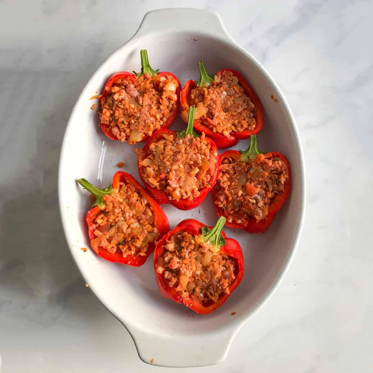 6 bell pepper halves filled with meat stuffing, in an oval baking pan