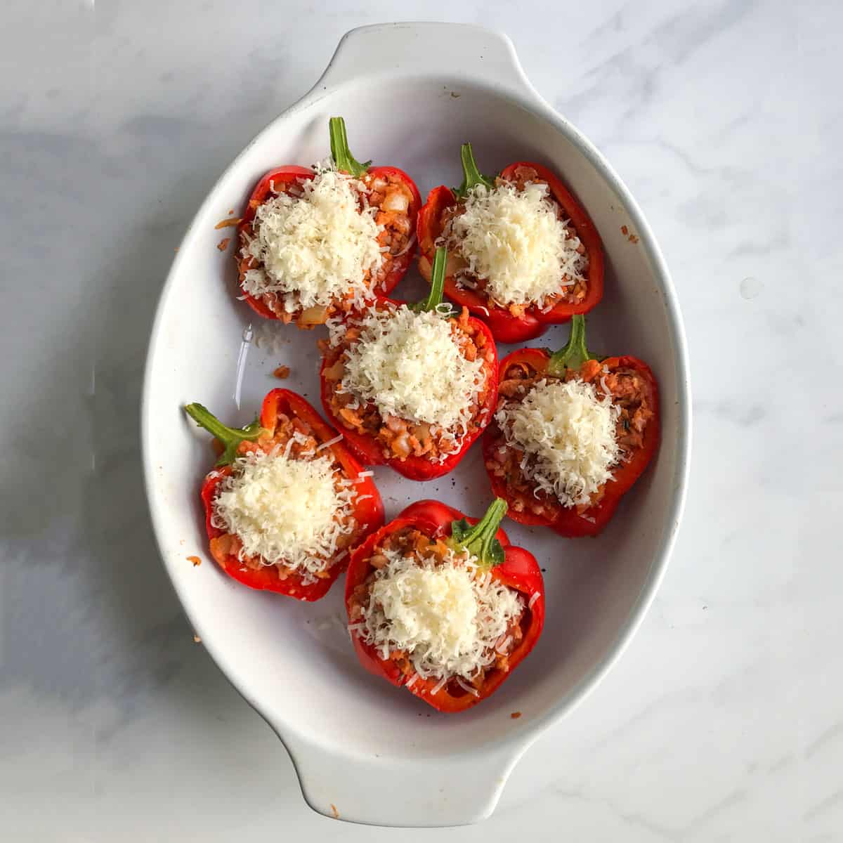 6 stuffed pepper halves in an oval baking pan, topped with grated parmesan cheese.