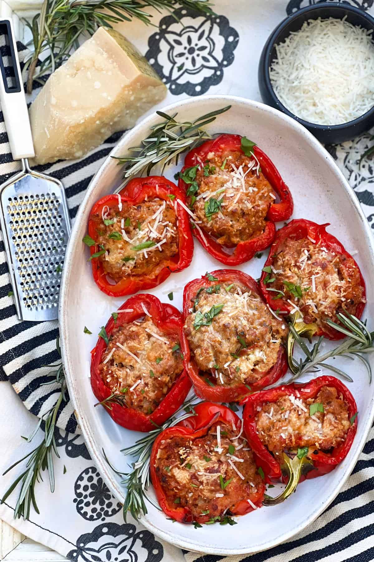 7 stuffed red bell pepper halves in a shallow oval serving bowl. A small bowl of grated parmesan on the side.