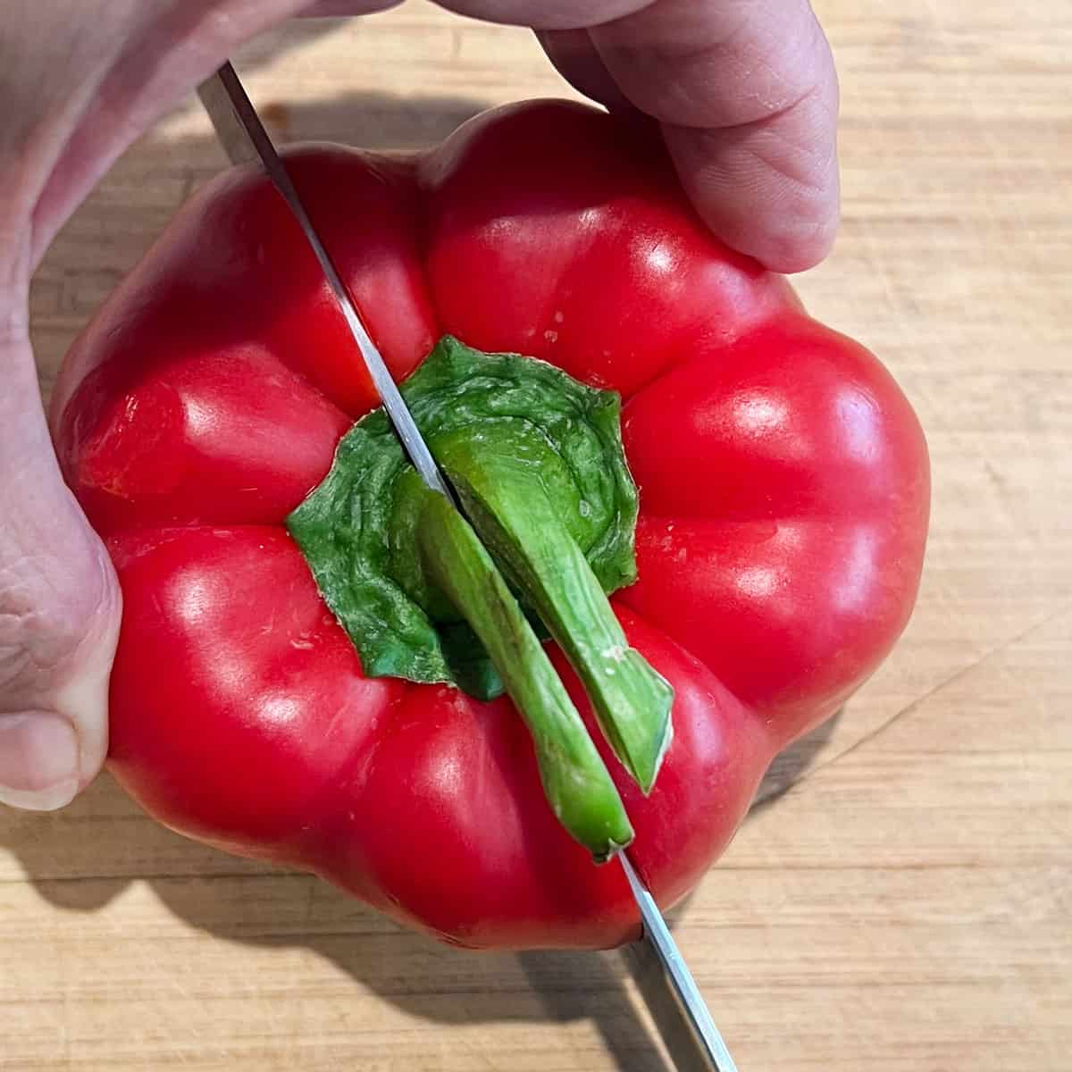 knife cutting a red bell pepper in half lengthwise through the stem.