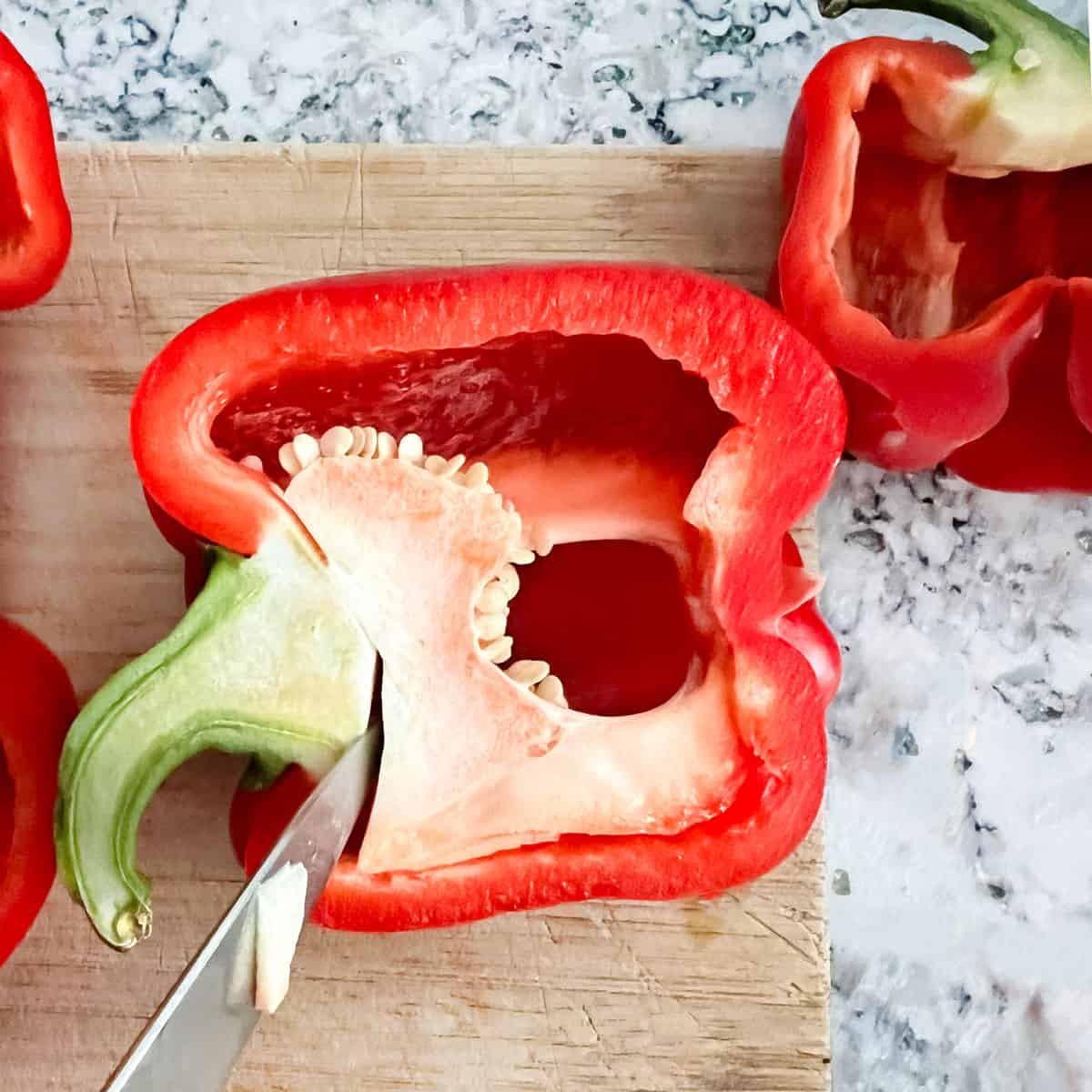 knife cutting the white pitch out of a halved raw red bell pepper