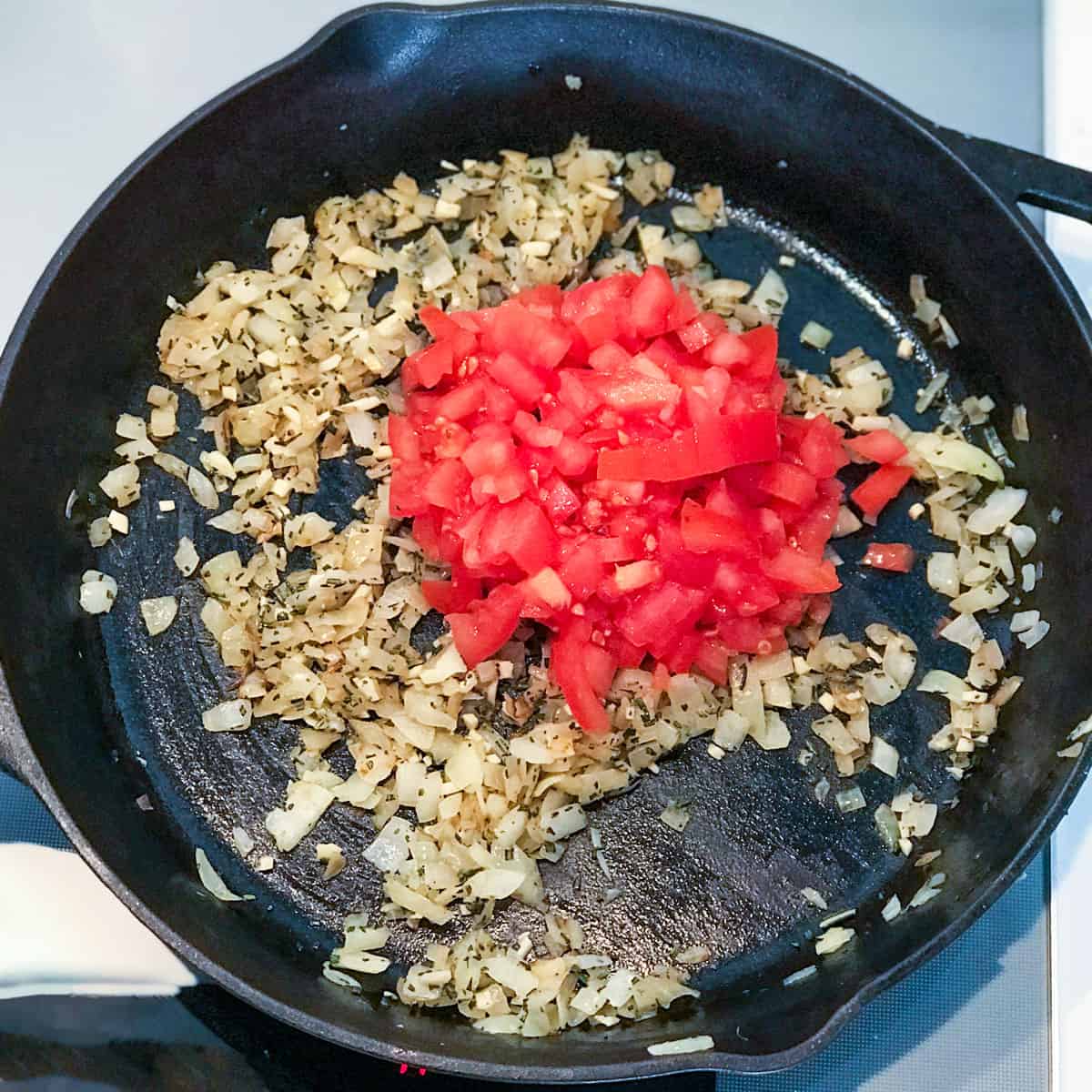 sauteed chopped onions in a cast iron skillet topped with chopped tomatoes and chopped rosemary.